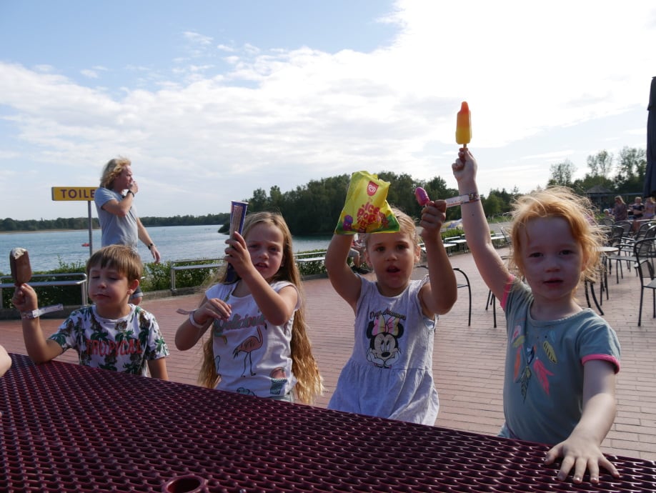 Kinderen steken vrolijk hun armen omhoog bij het water.