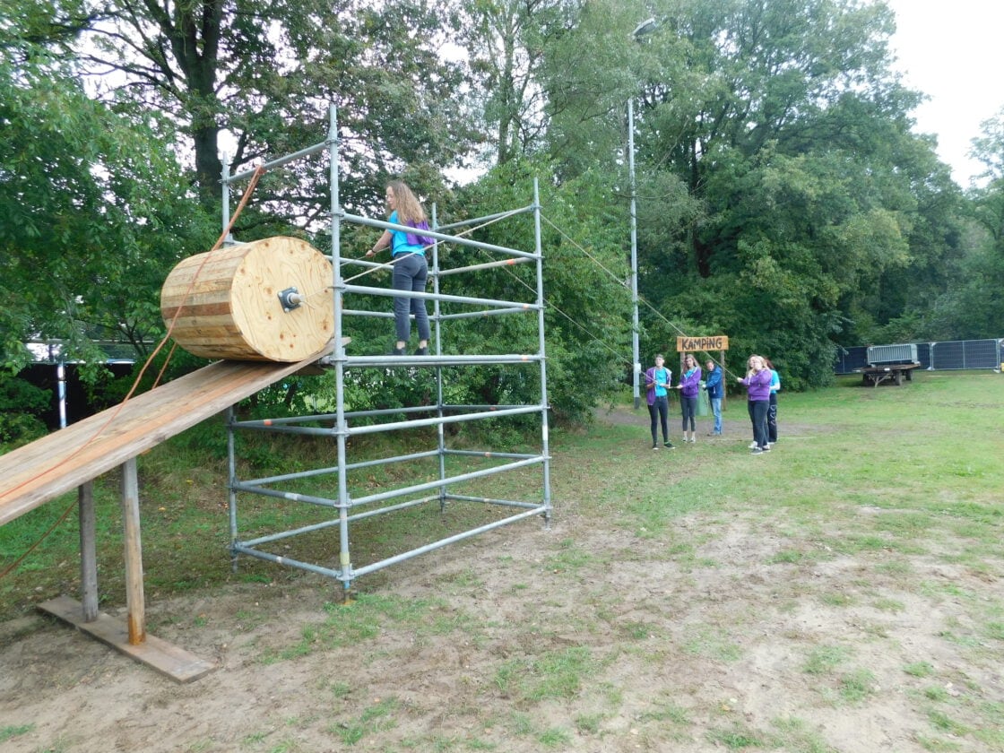Kinderen klauteren over een houten speltoestel op het veld.