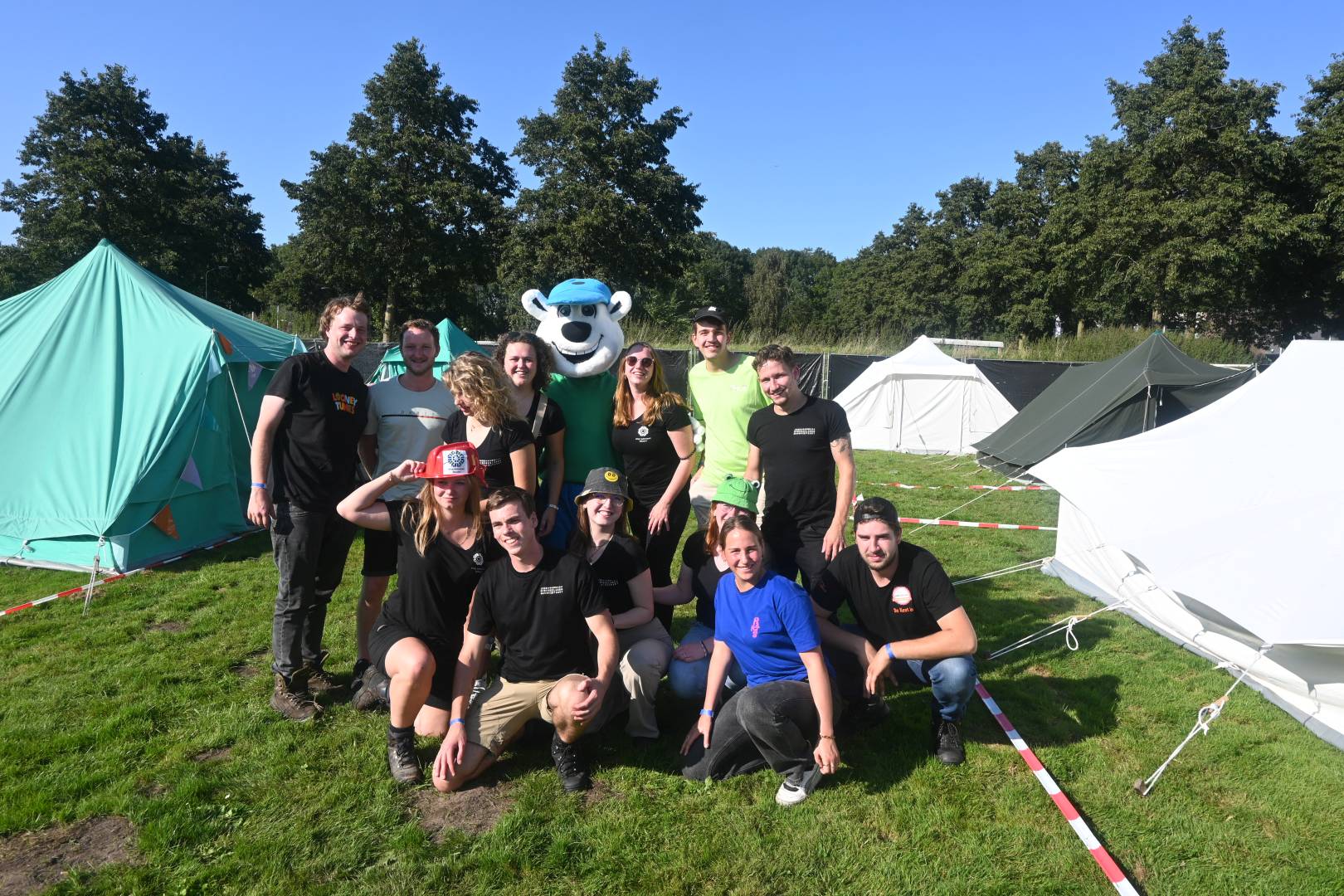 Een grote groep deelnemers zit samen op het gras voor de tenten.