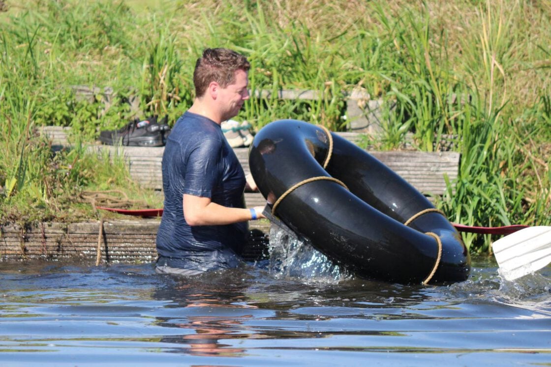 Een deelnemer staat met een rubberboot in het water tijdens een buitenspel.