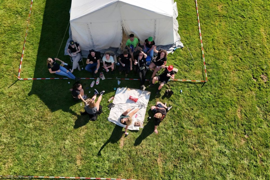 Deelnemers liggen samen in een kring op het gras, van bovenaf gezien.