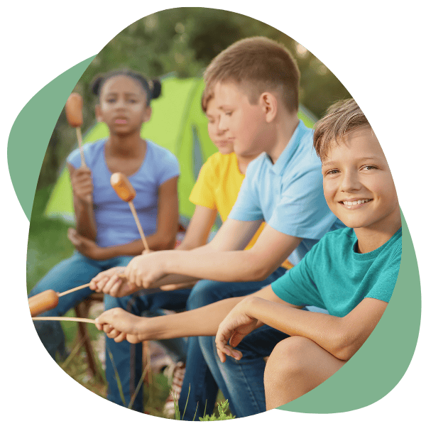 Kinderen roosteren samen knakworstjes bij de tent tijdens een kamp