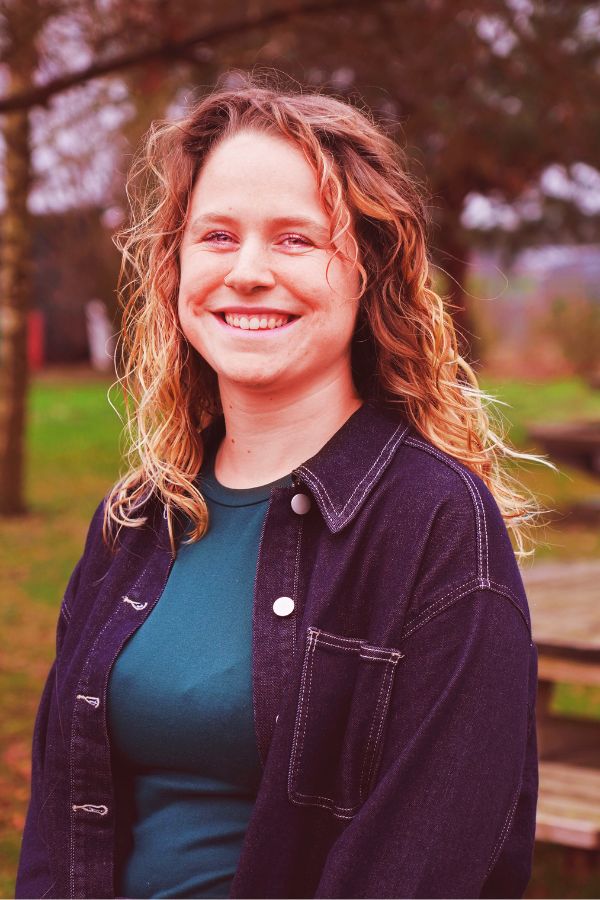 Sanne, vrijwilliger bij Jong Nederland, lacht buiten bij het clubterrein