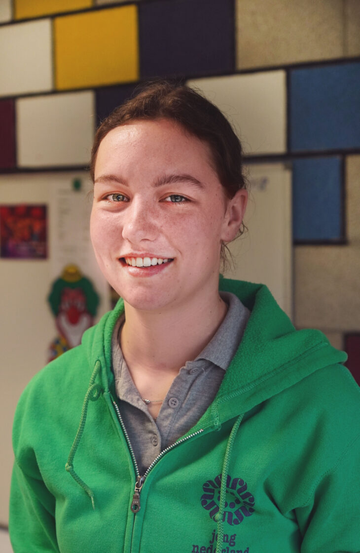 Jolanda, vrijwilliger bij Jong Nederland, lacht in een groene Jong Nederland trui in het clubhuis