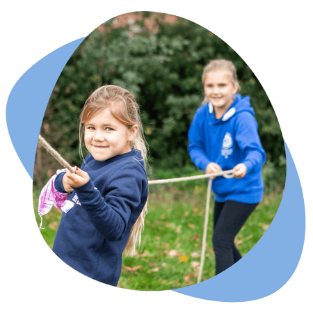 Twee meisjes in blauwe truien trekken samen aan een touw tijdens een buitenspel